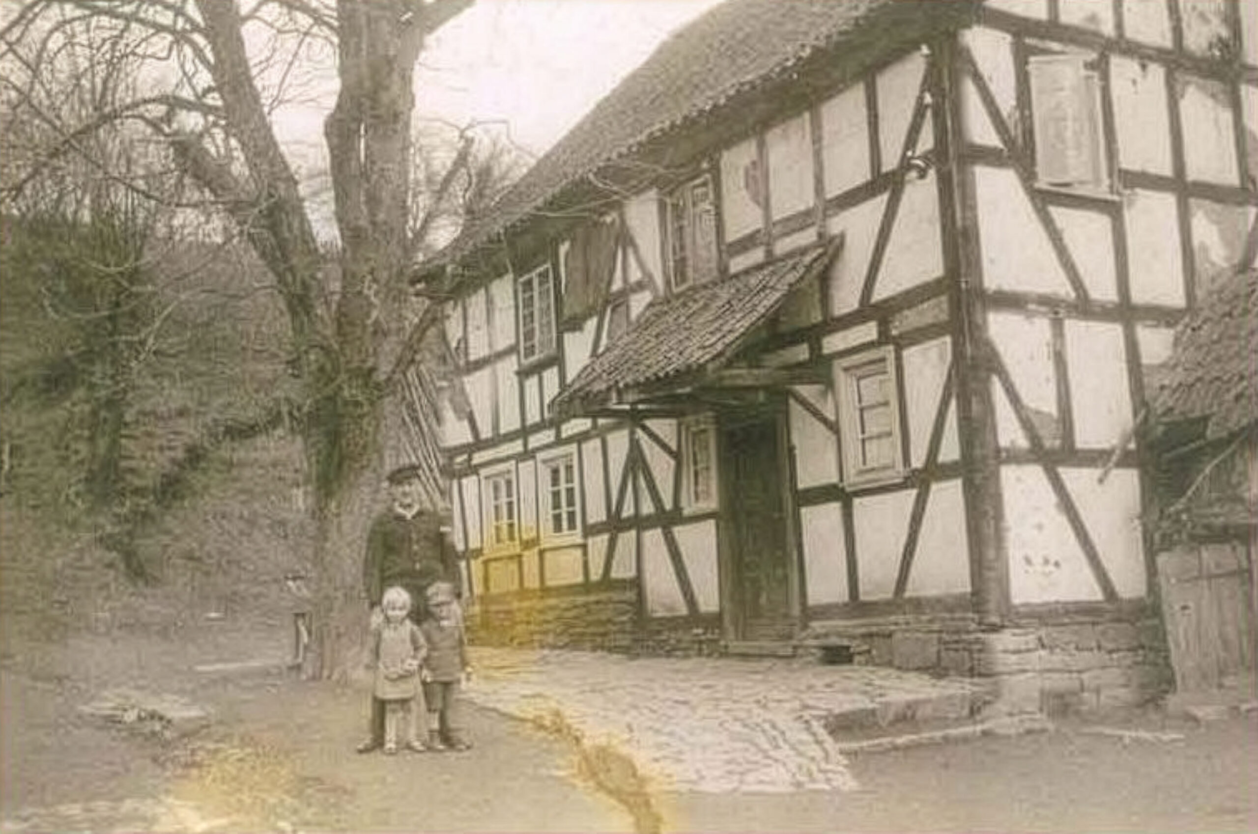 Historische Aufnahme eines Fachwerkhauses in Oberholpe mit zwei Kindern und einer erwachsenen Person in schlichter bergischer Alltagskleidung